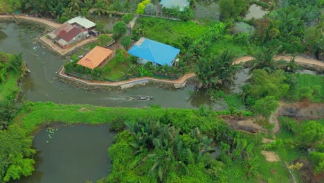 aerial drone view of peaceful countryside showing rural homes beside winding river and dense green vegetation, with tropical trees, ponds, and scattered houses in tranquil natural setting