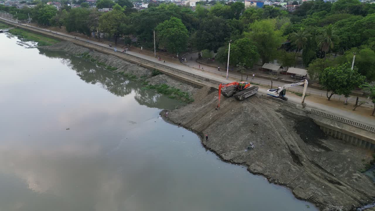 Escavatori su un cumulo di riempimento sulla strada lungo il fiume di Marikina City con alberi e attività veicolare durante il giorno nella Metro Manila, Filippine