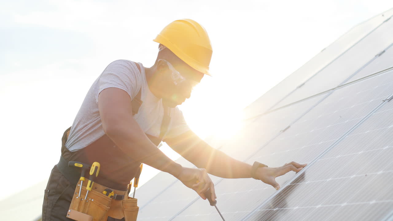 hombre afroamericano con uniforme especial y casco protector reparando un panel solar