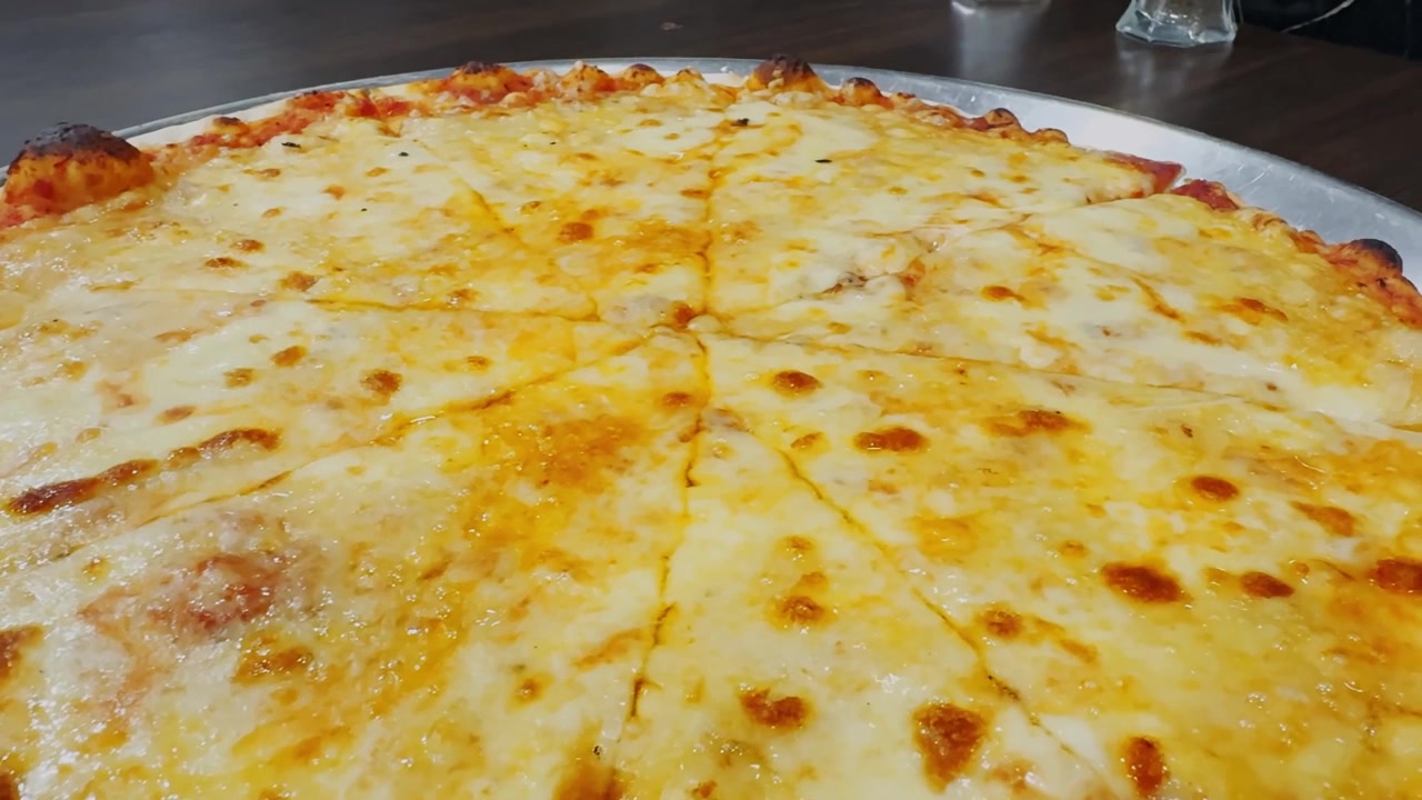 Pizza al formaggio su un vassoio di metallo con condimento dorato fuso, bordo di salsa di pomodoro, crosta cotta e bancone da cucina in acciaio inossidabile in un ambiente da ristorante.
