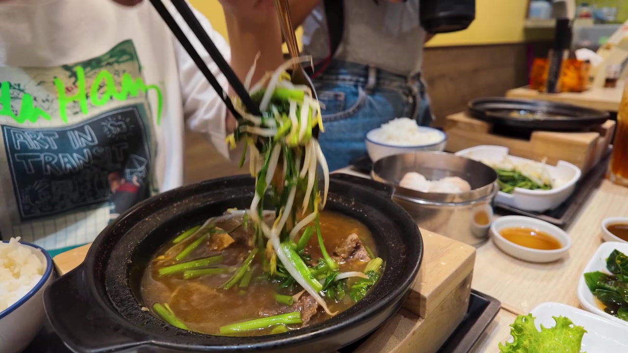 Primo piano di commensali che usano bacchette e cucchiai per mangiare stufato di manzo caldo a Bangkok.