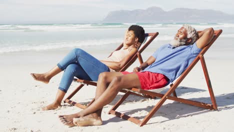 pareja afroamericana acostada en tumbonas en una playa soleada