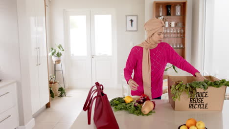 biracial woman in hijab with grocery shopping in kitchen at home with copy space, slow motion