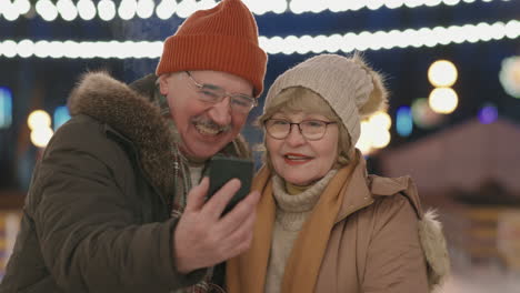 elderly couple taking selfie at night ice rink