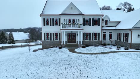 white two-story house adorned with red-bowed wreaths and snow-covered ground