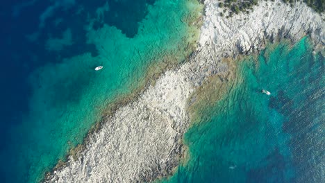 Top-down-view-boats-on-turquoise-clear-water,-rocky-peninsula-greek-island-Coastline