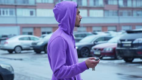 medium close up of young man wearing purple hoodie looking for car with key