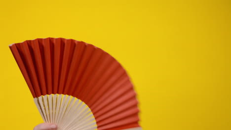 moving a red paper fan to create a gentle refreshing wind, then folding it and putting it down