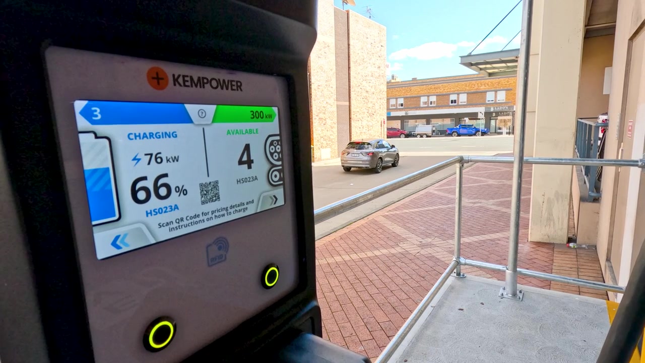 Primer plano de la pantalla de un cargador de vehículo eléctrico que muestra el porcentaje de batería y el estado de carga al aire libre.