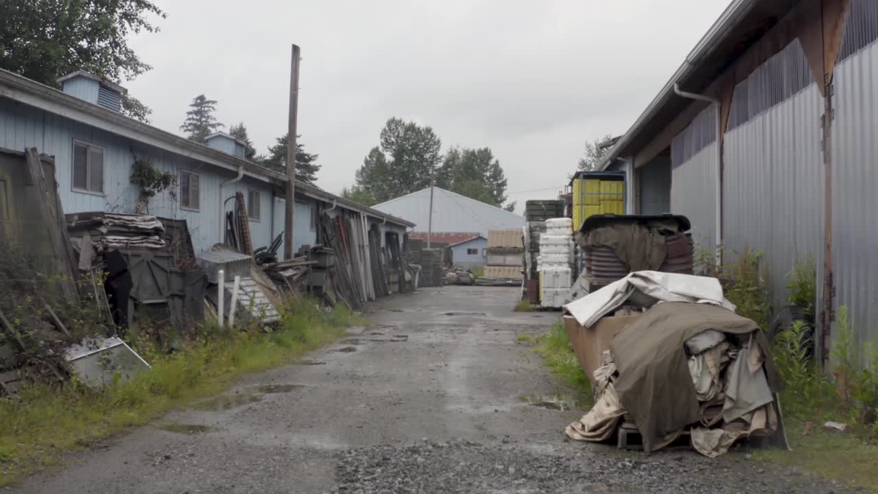 Aerial pan out of  Military storage building inbetween an alley of vintage and post modern parts on a rainy wet day with a aerial gradual rise.