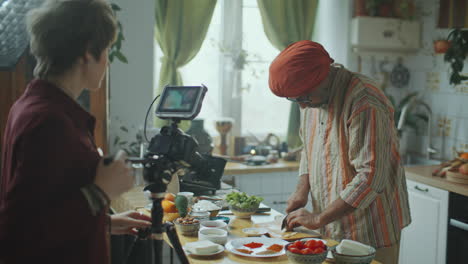 camerawoman filming indian food blogger chopping ingredients in kitchen