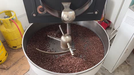 specialty coffee beans spinning on cooling and mixing tray in regular speed to reduce the heat evenly after roasting, production warehouse factory shot of food and beverage industry, tilt down shot