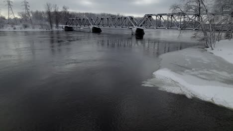 Old-frozen-railway-bridge-going-over-a-river-in-winter