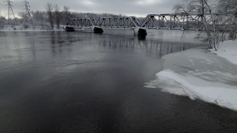old frozen railway bridge going over a river in winter