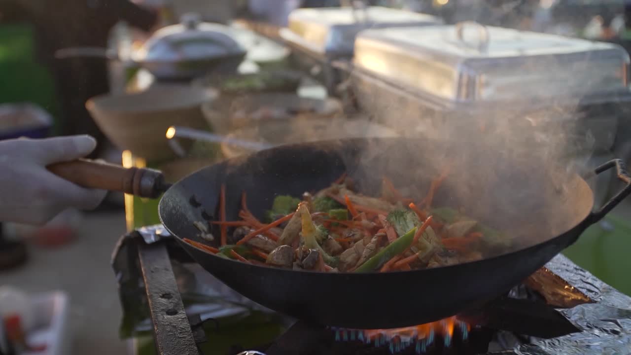 Primo piano di uno chef che cucina un pasto fresco in una padella wok in un mercato di strada marocchino.