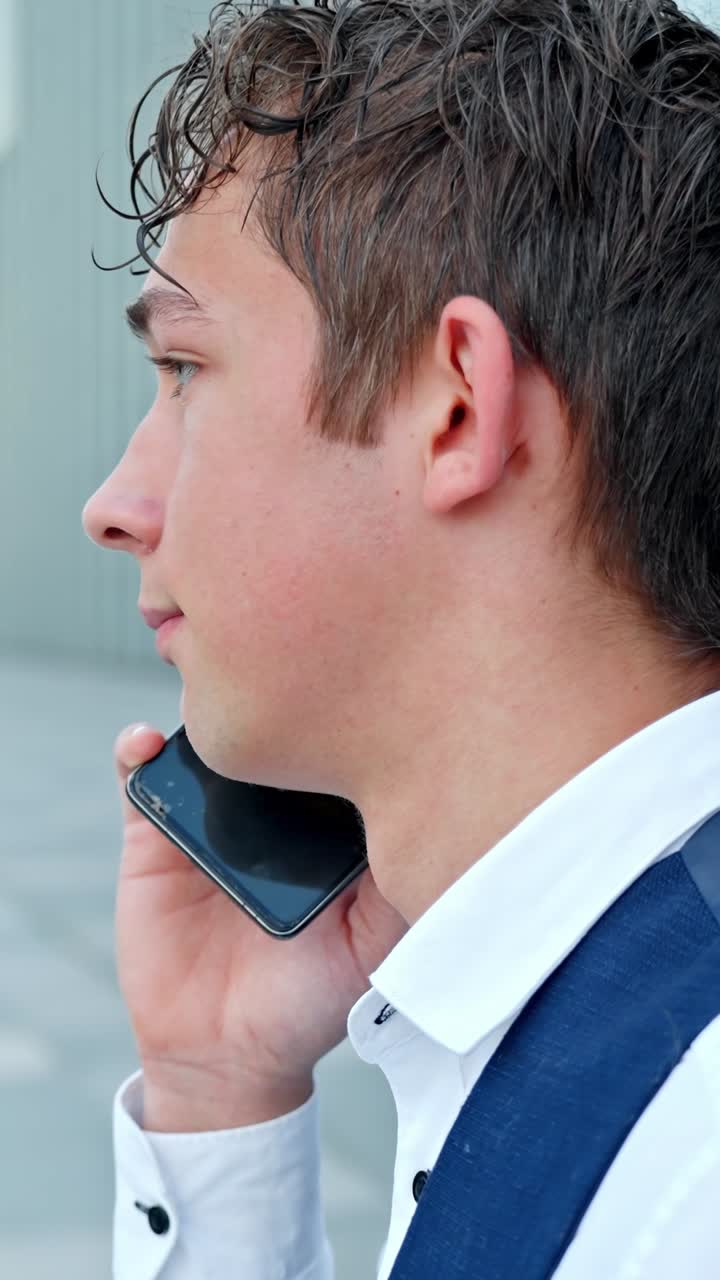 A vertical close-up shot circles around a young man in formal business attire speaking on his phone. The camera captures his face in detail as he talks