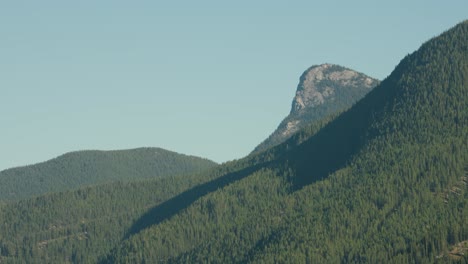 a long telephoto shot of the forest covered heart mountain range landscape against a blue summer sky in banff national park canada