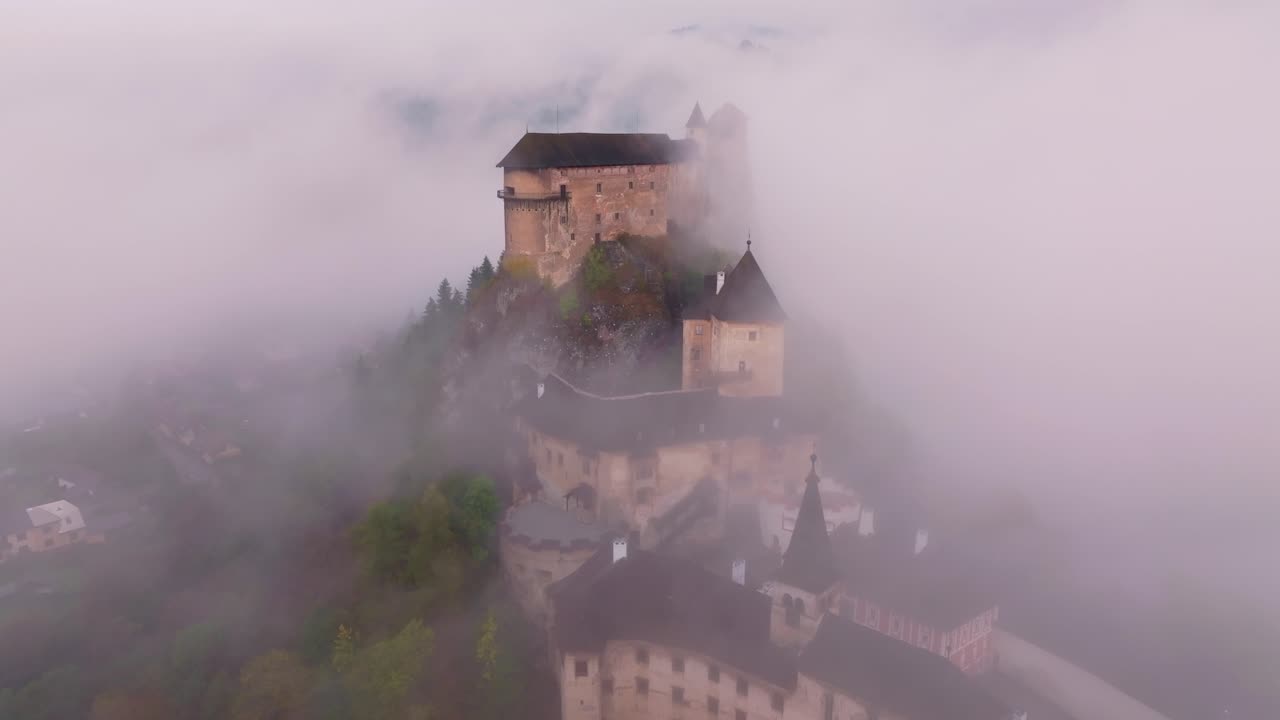 Ripresa con drone del Castello di Orava arroccato sopra nuvole mattutine alla deriva