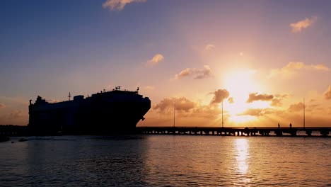 Silueta-De-Un-Buque-De-Carga-Para-El-Comercio-Internacional-Acercándose-Para-Atracar-En-El-Puerto-Durante-La-Hermosa-Puesta-De-Sol,-Plano-Amplio