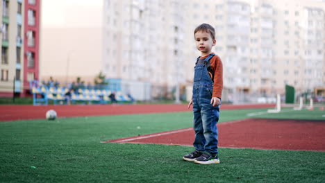 lovely baby boy runs to get his ball in the stadium. toddler playing sports game outdoors.