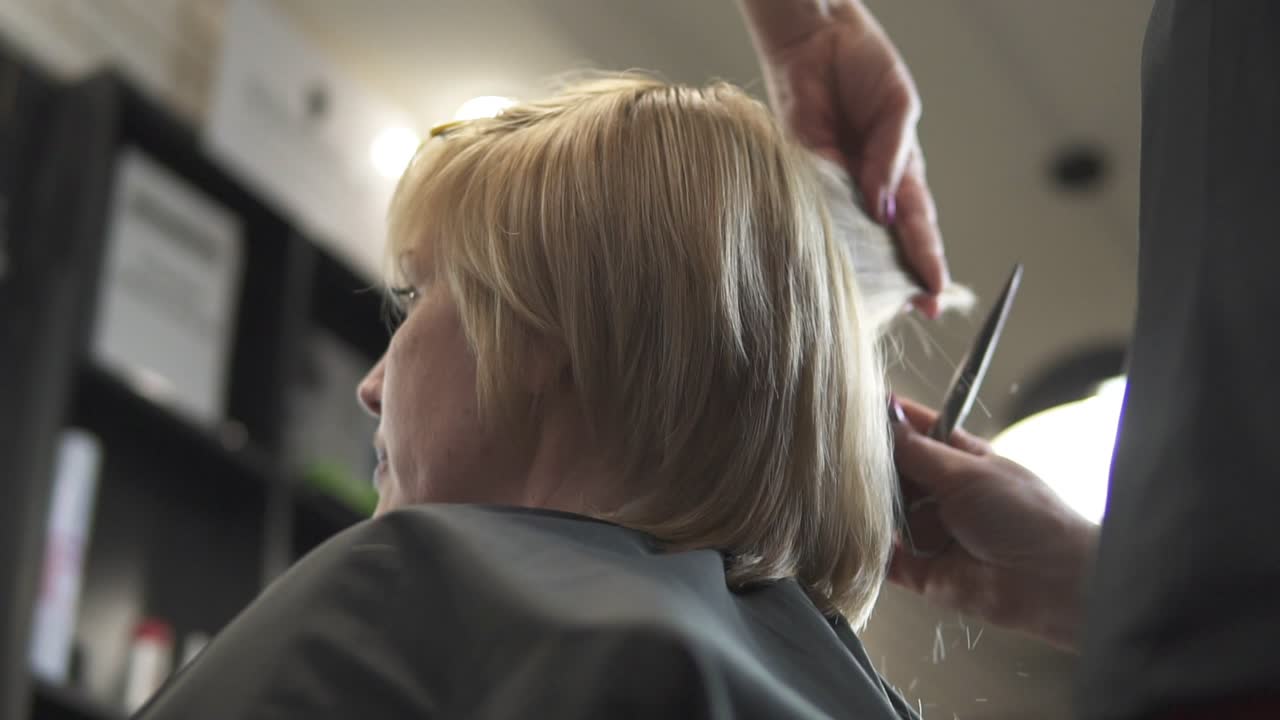 Young woman getting her hair dressed in hair salon. Close Up view of a hairdresser's hands cutting hair with scissors. shot in