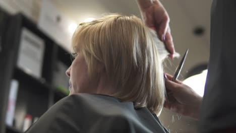 junge frau bekommt ihre haare im friseursalon angezogen. naheansicht der hände eines friseurs, der haare mit einer schere schneidet.