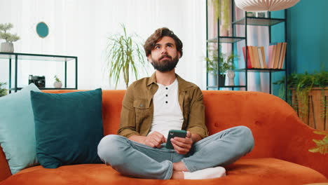 Middle eastern young man sitting on sofa using smartphone share messages on social media application