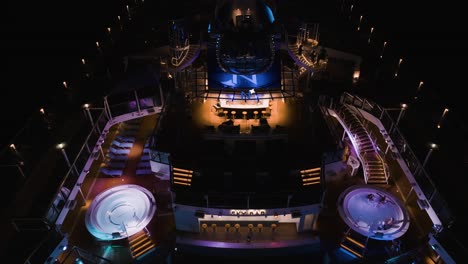 Un-Dron-Aéreo-Disparó-De-Arriba-Hacia-Abajo-Sobre-Las-Instalaciones-De-La-Piscina-De-La-Cubierta-Superior-Azul-Y-El-Jacuzzi-Sobre-Un-Enorme-Crucero-Por-La-Noche