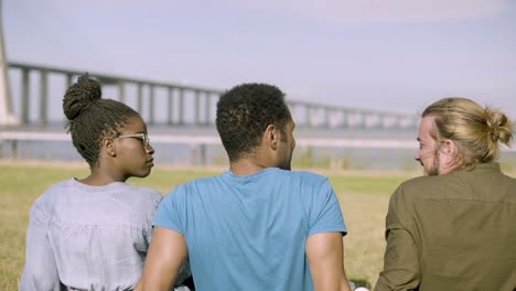 Cheerful-young-people-sitting-on-meadow-and-talking