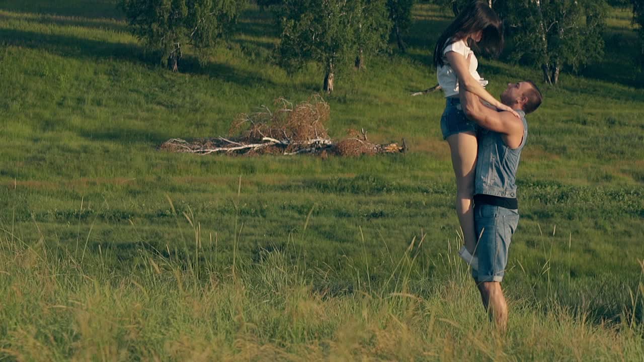 uma mulher jovem corre por um prado verde para um homem e salta para os braços