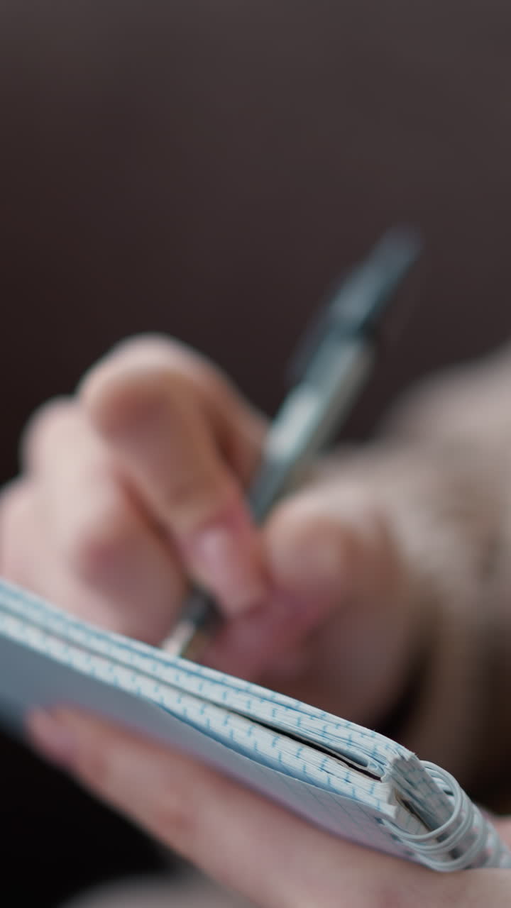 primer plano de la mano sosteniendo un bolígrafo y tomando notas en un cuaderno. el enfoque está en la escritura mientras que el fondo suave destaca un ambiente de estudio acogedor