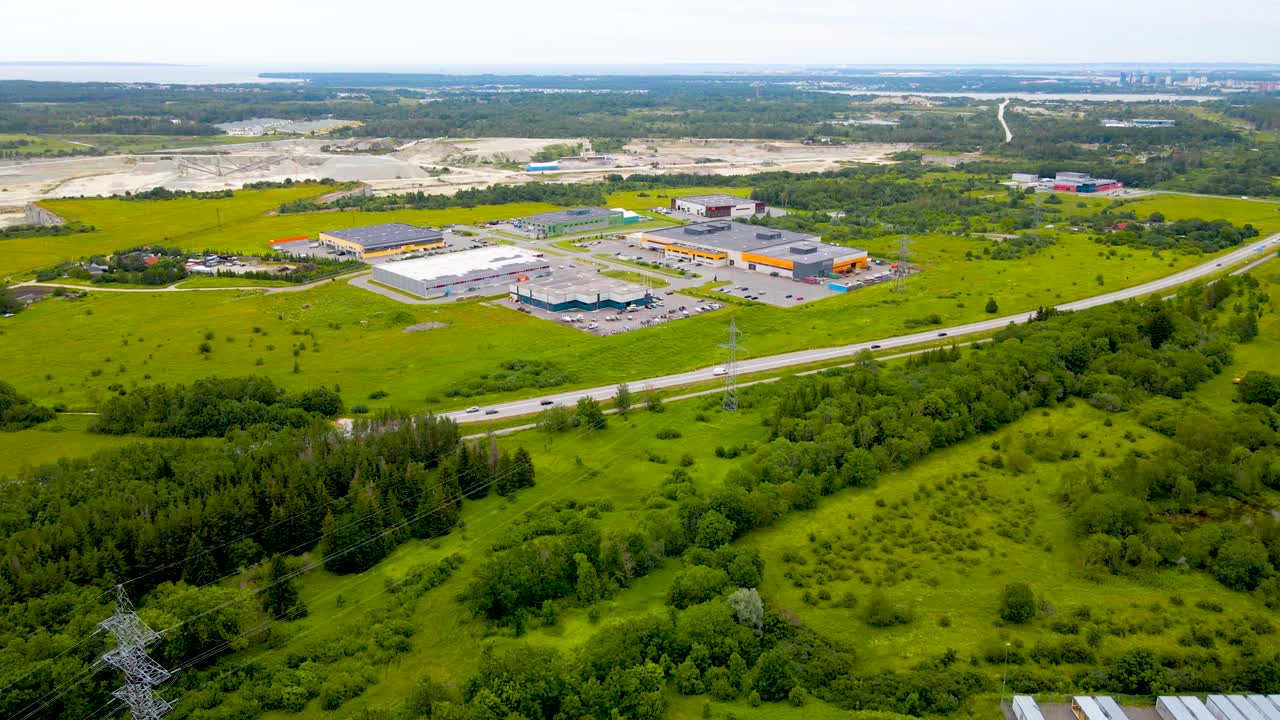 Aerial view over Tallinn-Paldiski highway at summer, Estonian national road. Roadway leads through the warehouse complex and gravel quarry, trees and green fields beside highway. Semi urban landscape
