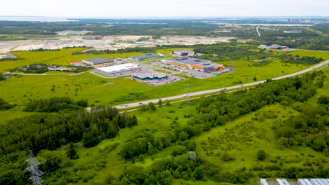 aerial view over tallinn-paldiski highway at summer, estonian national road. roadway leads through the warehouse complex and gravel quarry, trees and green fields beside highway. semi urban landscape