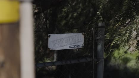 Worn-out-and-faded-associated-sign-hanging-on-a-chain-link-fence-while-a-tree-blows-its-leaves-in-front-of-it