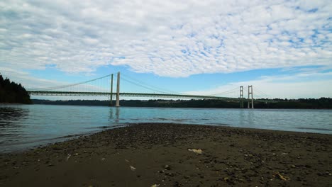 time lapse, hyperlapse, high stratus clouds streaming over puget sound and the tacoma narrows bridge, zoom in from a pebble and sand beach