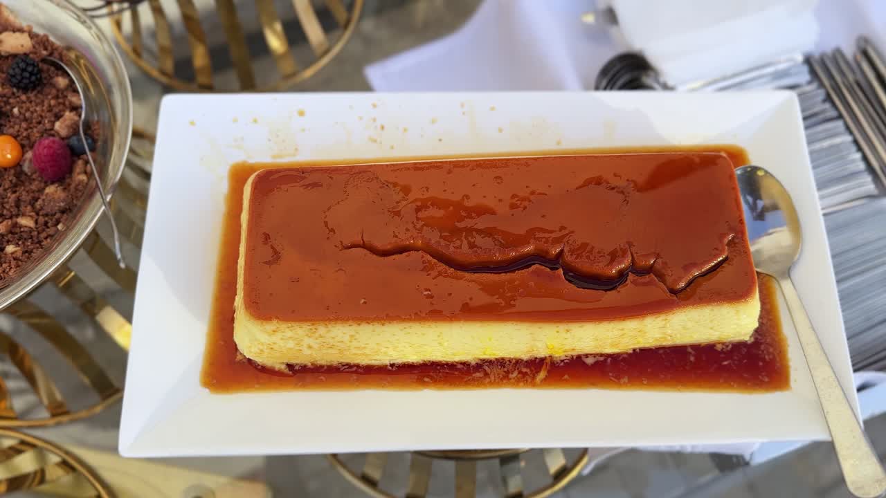 Nærbilde av karamellpudding (crème caramel) på et hvitt, rektangulært fat med blank karamellsaus og serveringsskje, buffetdessert-presentasjon for catering eller arrangement