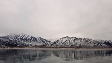 Tilt-up-shot,-revealing-frozen-Crowley-Lake-and-snowy-hills-and-mountain-in-winter