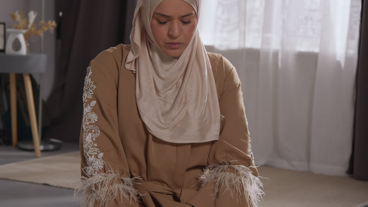 Muslimsk kvinde med hijab beder knælende på en bedemåtte derhjemme