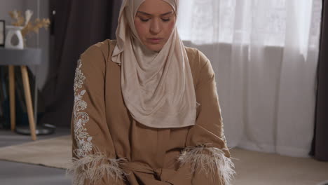 muslim woman wearing hijab at home praying kneeling on prayer mat 2