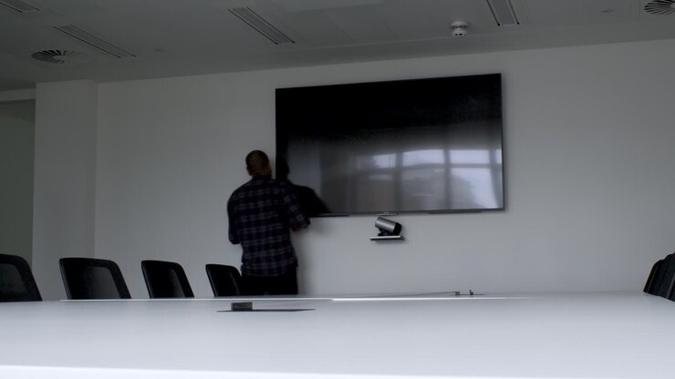 A static shot of a man trying to turn on the monitor in a conference room