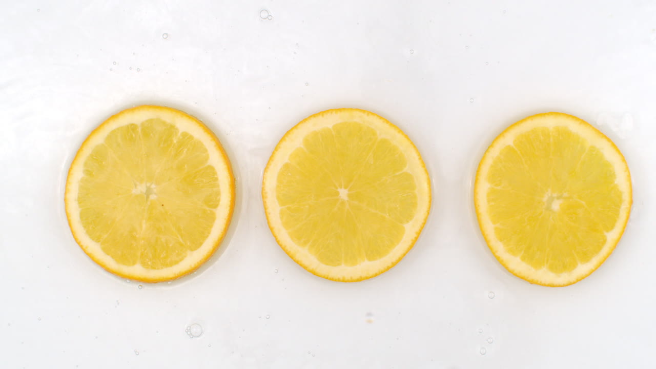 Top view: on a white background a three fresh orange is lying in the water water drops are falling from above and splashes are falling in slow motion in all directions.