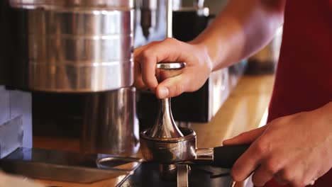 waiter using a tamper to press ground coffee into a portafilter