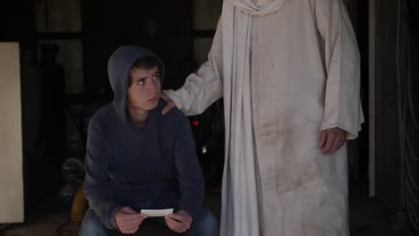 Jesus,-wearing-a-white-robe-that-is-dirty-and-tattered,-offers-his-hand-in-comfort-to-a-sad-and-lonely-looking-teenage-boy