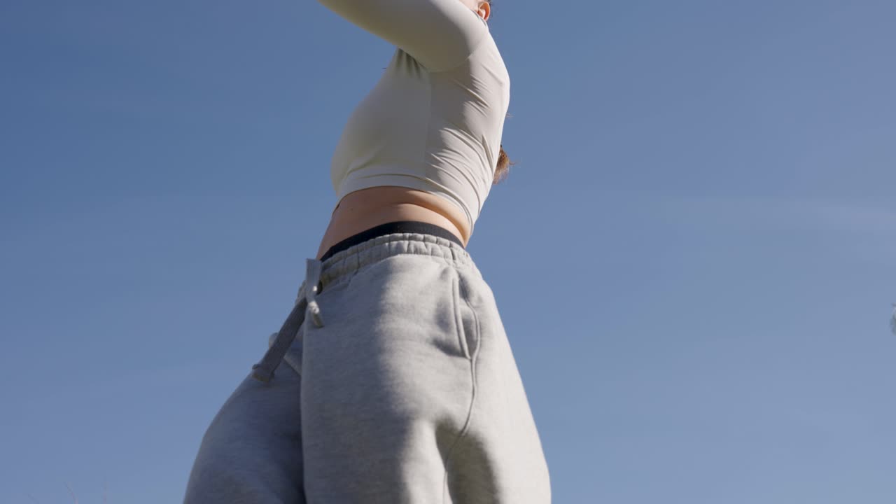 Young woman performing modern dance outdoors against blue sky