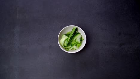 hand grabs bowl of sliced cucumber. overhead shot