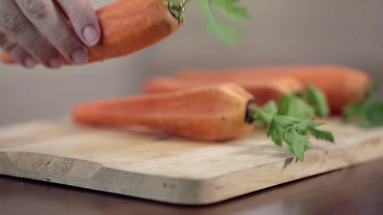 Mano che posiziona carote fresche su un tagliere di legno