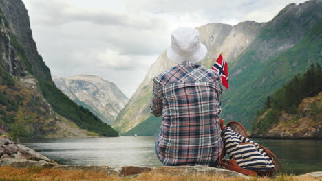 turista con mochila y bandera de noruega admira el grandioso turismo de fiordos en escandinavia concepto 4k v