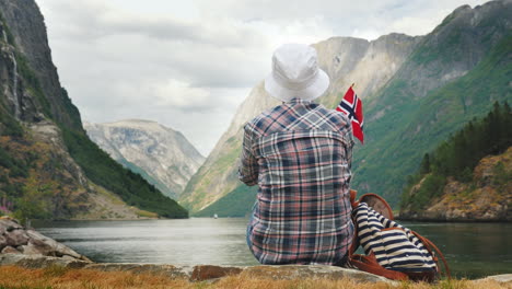 tourist with backpack and flag of norway admires grandiose fjord tourism in scandinavia concept 4k v