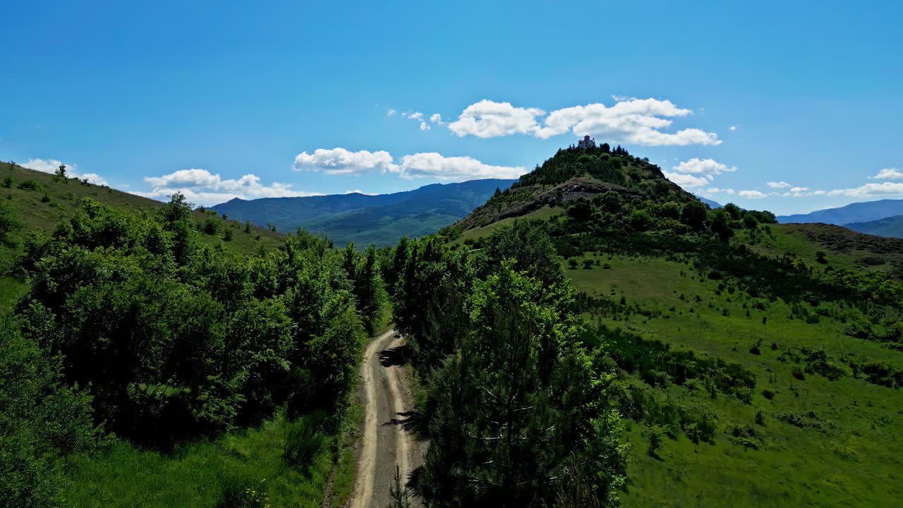 el dron se eleva por encima de un sinuoso camino de tierra enclavado entre montañas, con vistas a los exuberantes prados verdes de grecia.
