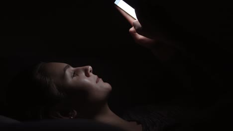 closeup view of a woman laying on a couch and using her phone in a dark room, chatting in the darkness with smartphone, communicating with friends online